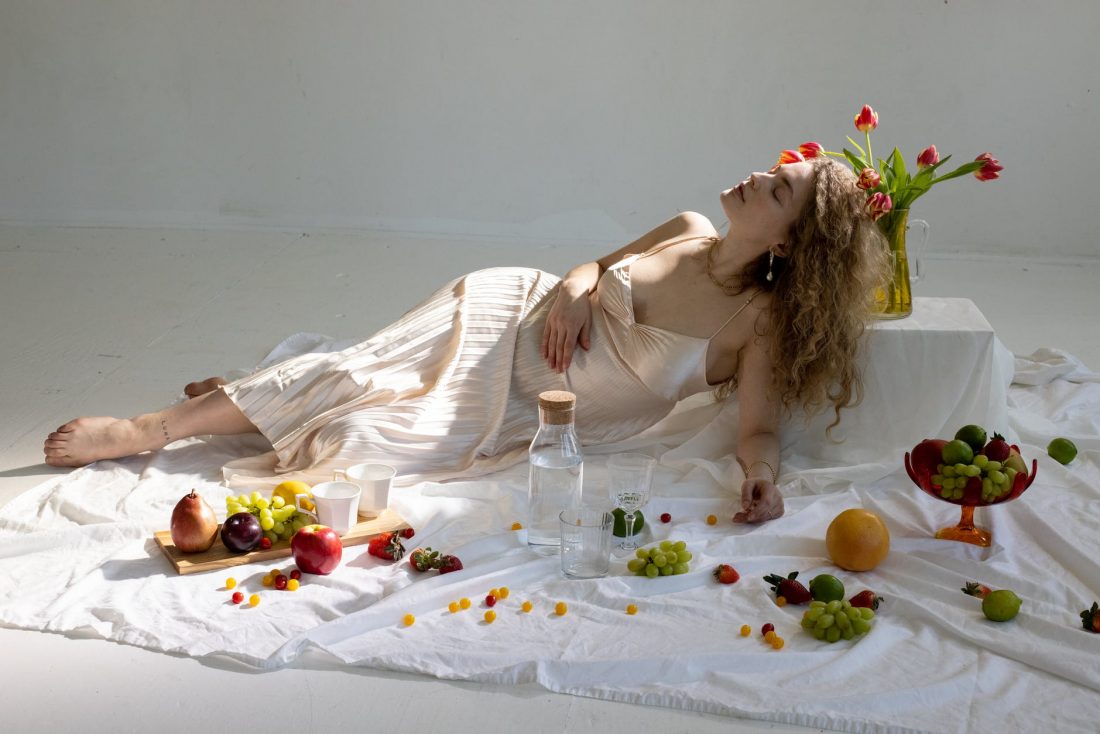 peaceful young elegant woman lying on floor near fruits scattered on white cloth