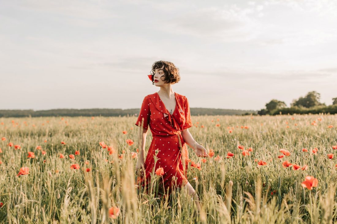 woman in a red dress standing in the middle of a poppy flower field