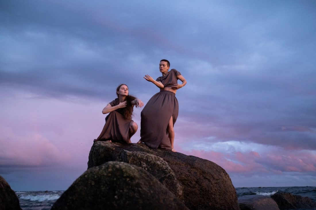 women in brown dress dancing on brown rock on a shore